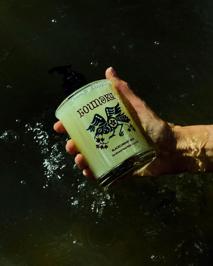 Hand holding a bottle labeled 'Blackcurrent Bud' over water